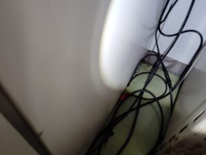 千代田区の歯科医院にて、簡易キッチンの壁の角に電源コードや通信配線が集まる場所を精密調査。配線の隙間に、ゴキブリの糞が散見される様子