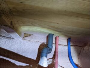 床下側から給排水管が床を貫通している箇所を一つずつ目視点検し、ミリ単位の隙間やパテの劣化がないか確認するプロの調査風景