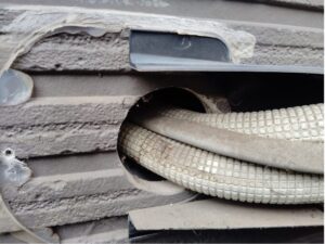 品川区の戸建て住宅、外壁側のエアコン配管貫通部でひび割れ・剥がれが生じた古いパテの劣化状況